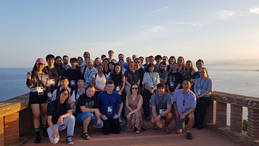 A group of 50 people standing in front of a stone barrier with the sea in the background