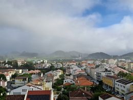 Photo showing roofs of houses with morning mist hanging over mountains in the background